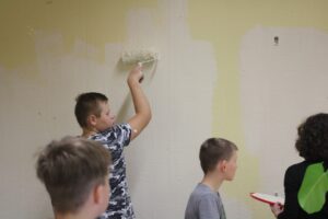 Schüler streichen eine Wand in einem Klassenraum.