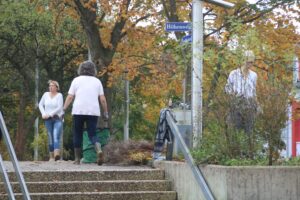 Zwei Personen gehen eine Treppe hinunter, Laub und Straßenbeschilderung im Hintergrund.