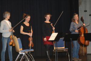 Vier Musikerinnen mit Streichinstrumenten stehen auf einer Bühne.