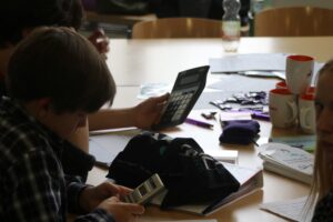 Schüler mit Taschenrechner und Handy an einem Tisch, umgeben von Schulmaterialien.