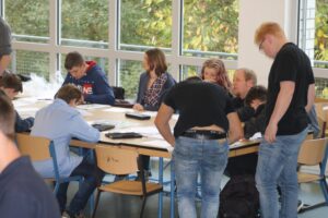 Gruppendiskussion an einem Tisch mit Schülern und Lehrern in einem Klassenraum.