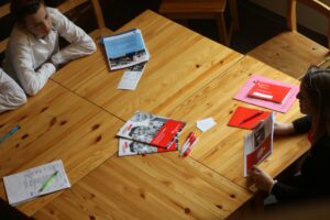 Zwei Personen sitzen an einem Holztisch mit Unterlagen und Broschüren.