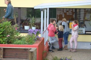 Kinder essen Eis und stehen vor einem Fenster. Pflanzen und Blumen sind im Vordergrund.