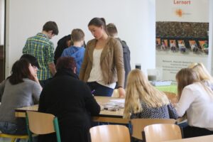 Schüler arbeiten an Tischen, einige stehen und unterhalten sich.