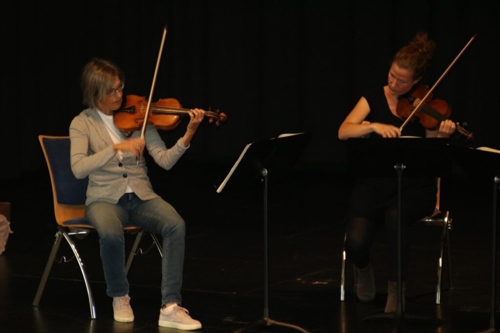 Zwei Musikerinnen spielen Geige auf einer Bühne.