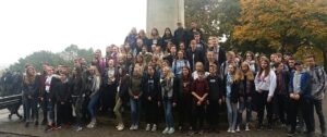 Gruppe von Schülern posiert vor einem Denkmal im Freien an einem bewölkten Tag.