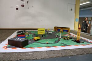 Modell einer Baustelle mit Fahrzeugen und Hinweisschildern auf grünem Untergrund.