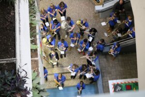 Schüler in blauen T-Shirts spielen Instrumente in einem Innenhof.