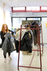 Schülerin hängt Jacken an ein Kleidergestell in einem Klassenraum.