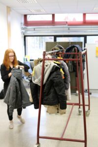 Schülerin hängt Jacken an einem Kleiderständer im Klassenraum auf.