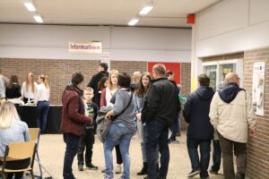 Schüler und Eltern interagieren in einem Flur mit Informationsständen.
