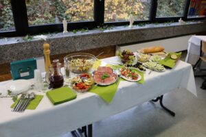 Buffet mit verschiedenen Salaten, Brot und Getränken auf einem gedeckten Tisch.