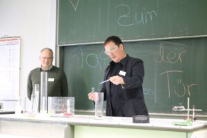 Zwei Männer führen ein Experiment am Tisch in einem Klassenzimmer durch.