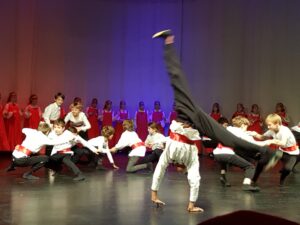Tanzgruppe mit Kindern in roten und schwarzen Kostümen auf einer Bühne.