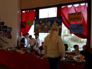 Eine Gruppe von Schülern am Buffet mit traditionellen Speisen. Rote Vorhänge im Hintergrund.