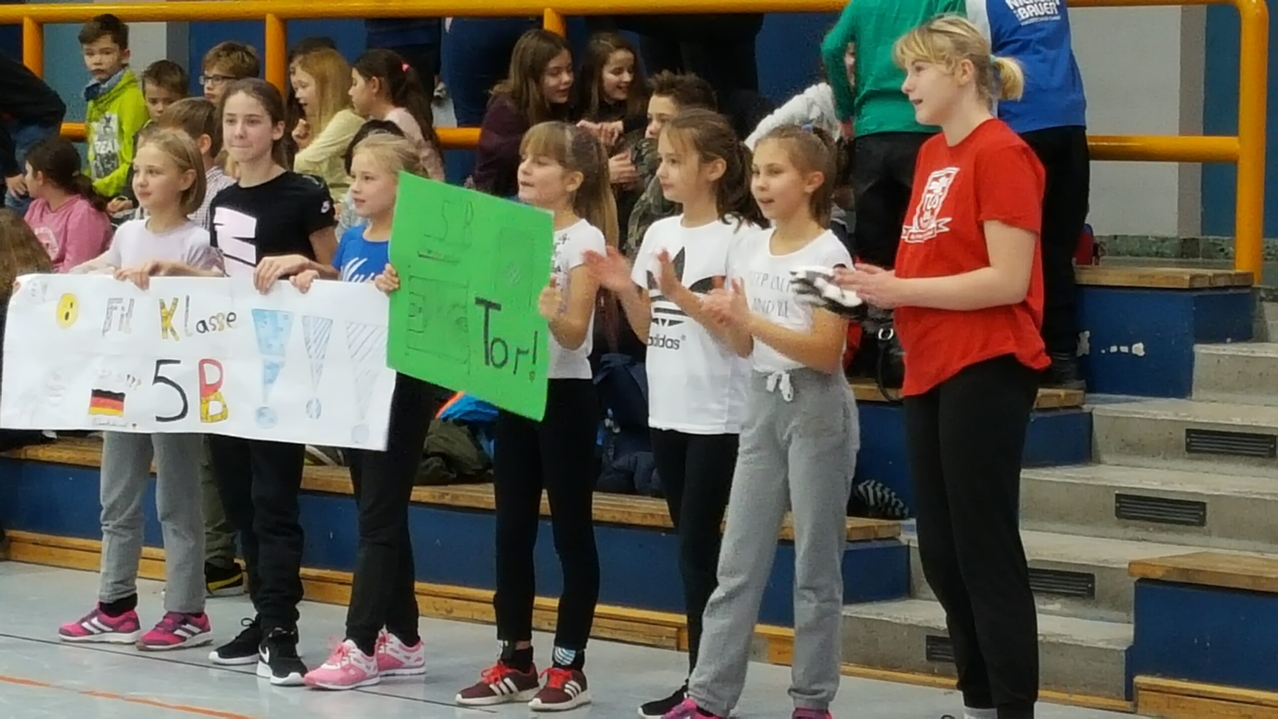 Mädchen stehen in einer Sporthalle mit Schildern und jubeln.