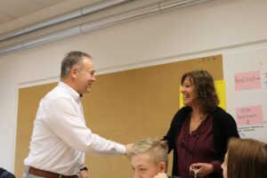 Eine Lehrerin und ein Lehrer unterhalten sich lächelnd in einem Klassenzimmer.