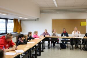 Schülerinnen und Schüler sitzen an einem Tisch in einem Klassenzimmer.