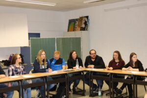 Eine Gruppe von Menschen sitzt an einem Tisch in einem Klassenraum.