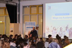 Vortrag in einer Aula mit Schülern und Präsentation über Auslandsaufenthalte.