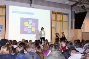 Schülerin präsentiert vor Publikum mit bunten Post-it-Zetteln auf der Leinwand.