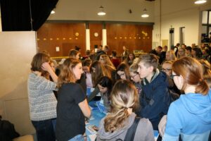 Schülerinnen und Schüler stehen an einem Tisch und sprechen miteinander.
