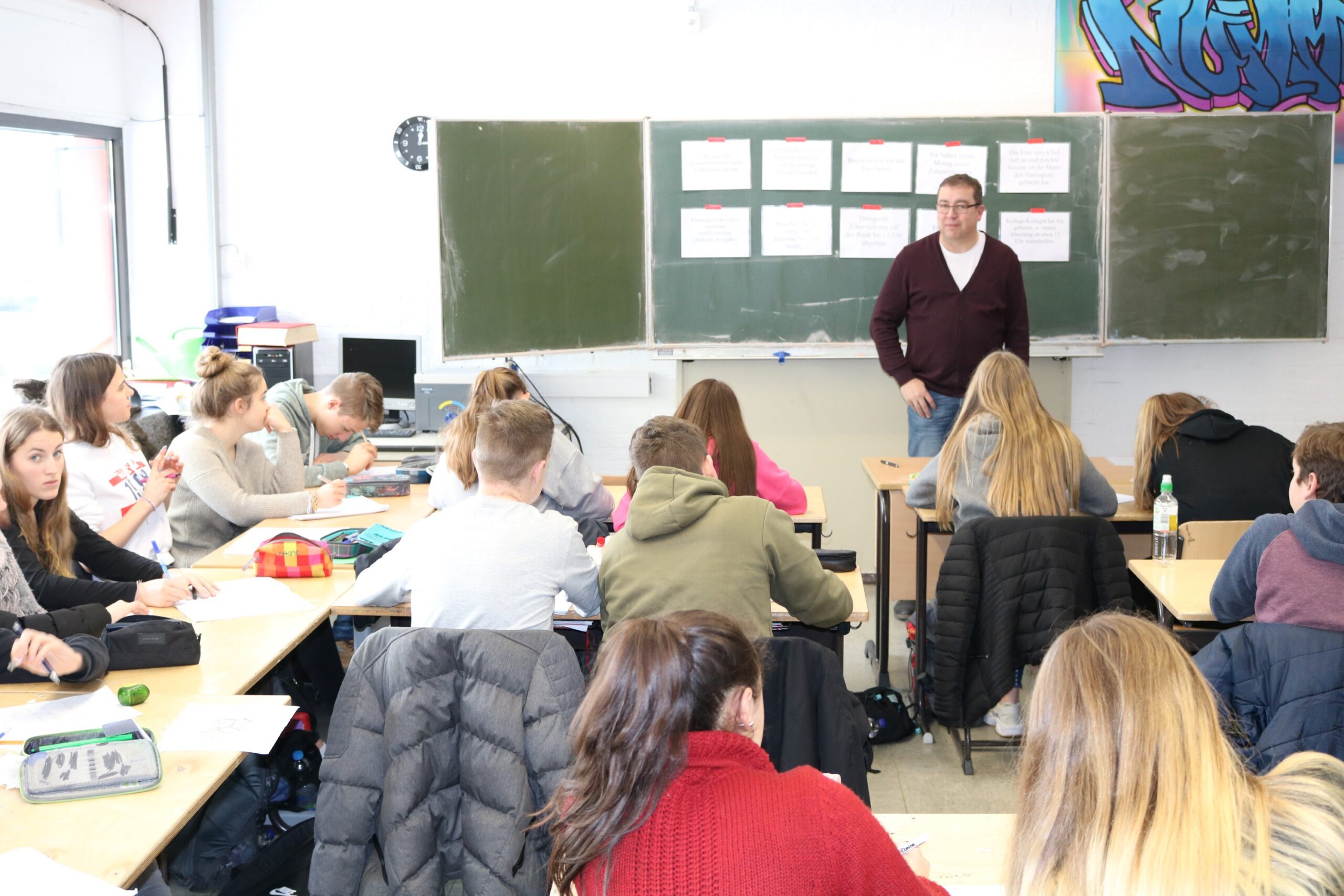 Lehrer spricht vor einer Schülergruppe in einem Klassenzimmer.