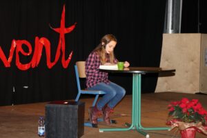 Ein Mädchen sitzt an einem Tisch und liest. Im Hintergrund steht das Wort "Advent".