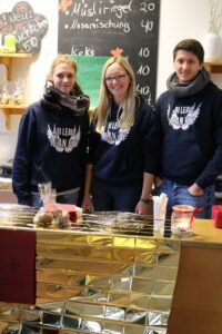 Drei Personen stehen an einem Thekenbereich mit Schiefertafel und Dekoration.
