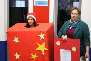 Mädchen in Geschenkbox mit Weihnachtsmütze und Frau mit Plakat.