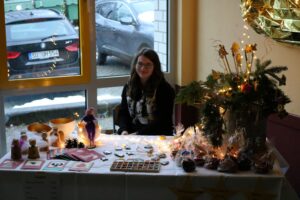 Frau sitzt an einem dekorierten Stand mit Gebäck und Weihnachtsdekoration.