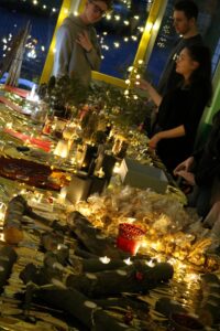 Weihnachtsmarkt mit festlich dekorierten Tischen und Lichtern. Besucher stehen zusammen.