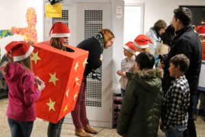 Gruppen von Kindern und Erwachsenen in Weihnachtsmützen, die an einem Stand stehen.