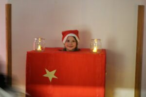 Kind in rotem Geschenk mit Weihnachtsmütze, Kerzen auf beiden Seiten.