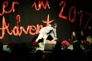 Theateraufführung mit Schauspielern auf der Bühne und festlicher Dekoration.
