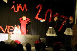 Aufführung auf einer Bühne mit drei Schauspielerinnen und Dekoration in Rot.