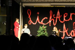 Aufführung auf einer Bühne mit Schauspielern und Weihnachtsbaum im Hintergrund.