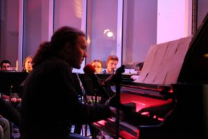 Junger Musiker am Piano während eines Auftritts, Publikum im Hintergrund.