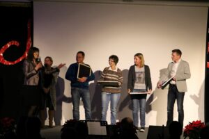 Eine Gruppe von fünf Personen steht auf einer Bühne, lächelnd und in Gespräch vertieft.