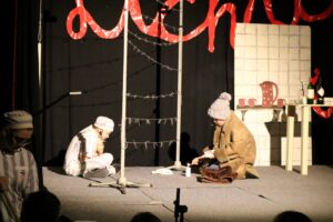 Theateraufführung mit zwei Schauspielern auf der Bühne, eine Weichnachtsbaum und Requisiten.