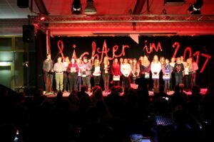 Schüler stehen auf einer Bühne bei einer Veranstaltung mit rotem Licht.