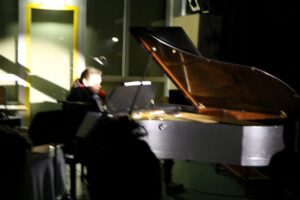 Ein Pianist spielt an einem Klavier in einem schwach beleuchteten Raum.