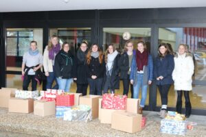 Gruppe von Frauen steht neben Geschenkkisten vor einem Gebäude.
