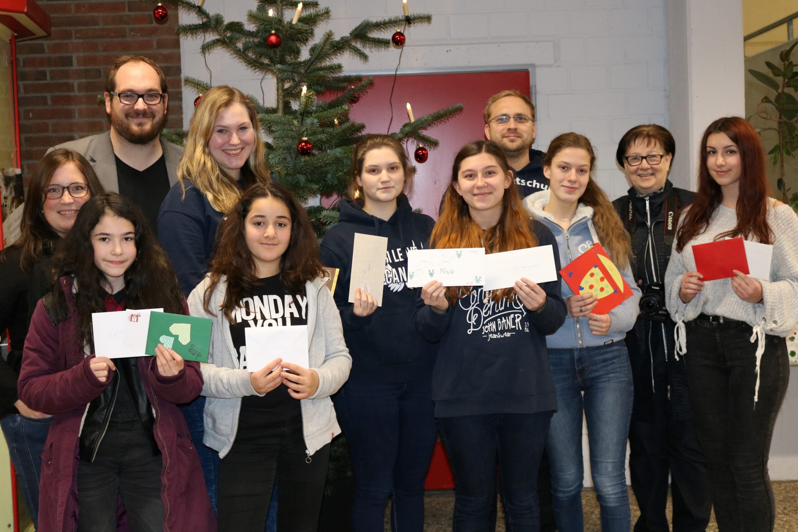 Gruppe von Schülerinnen und Schülern mit Weihnachtskarten vor einem geschmückten Tannenbaum.