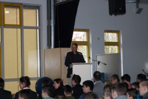 Ein Redner steht vor einem Publikum in einem Klassenraum.