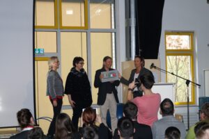 Eine Gruppe von vier Personen steht auf einer Bühne und hält eine Auszeichnung.