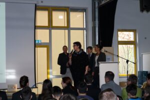 Präsentation vor Publikum in einem hellen Raum mit mehreren Personen am Podium.
