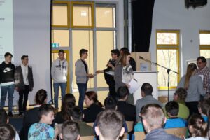 Schüler erhalten Preise auf einer Schulveranstaltung. Publikum schaut zu.