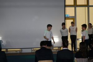 Schüler führen auf einer Bühne vor einer Leinwand eine Aufführung auf.