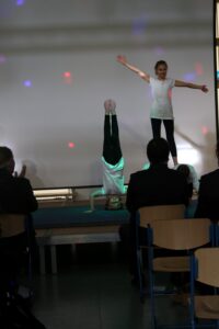 Schülerin präsentiert eine Akrobatiknummer auf der Bühne. Publikum applaudiert.